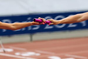 Passage de témoin rose entre deux coureurs lors d'une course de relais en athlétisme