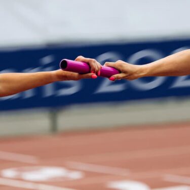 Passage de témoin rose entre deux coureurs lors d'une course de relais en athlétisme