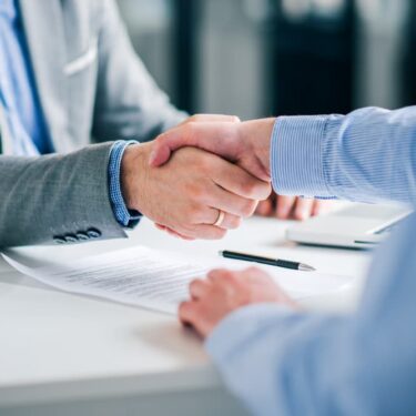 Deux professionnels se serrant la main lors d'une réunion d'affaires, avec des documents contractuels et un stylo sur la table.