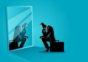 Homme d'affaires assis, pensif, regardant son reflet dans un miroir, sur fond bleu uni.