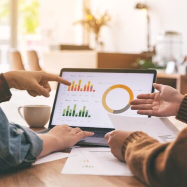 Deux professionnels analysent des graphiques de données financières sur un écran d'ordinateur portable.