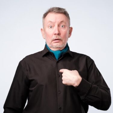 Homme d'âge mûr se désignant du doigt avec un air surpris, illustrant la notion d'intuitu personae